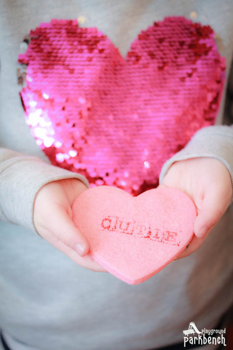 Pink heart sugar cookies stamped with conversation heart messages in a child's hands